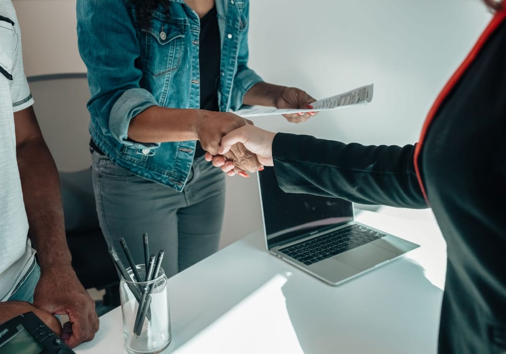 Two people shaking hands over paperwork in an office