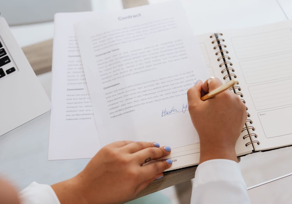 A hand signing a contract at a desk
